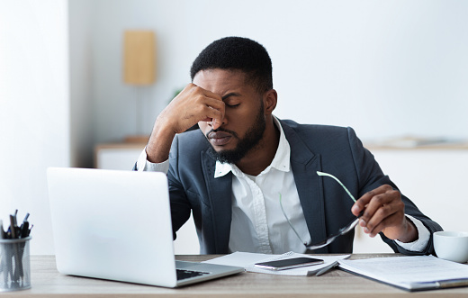 African businessman massaging his nose bridge, tired of long time work on laptop, copy space