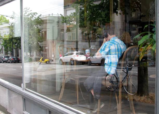 Vancouver, Canada - August 3, 2016: Teenage boy at downtown Finch’s Tea & Coffee House having lunch seen through the glass of window and reflection of the city live.