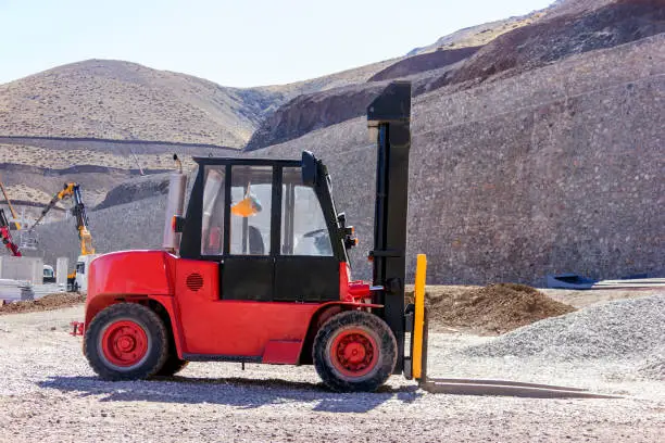 An old red and black colored forklift in the construction site. A forklift (also called lift truck, jitney, fork truck, fork hoist, and forklift truck) is a powered industrial truck used to lift and move materials over short distances.
