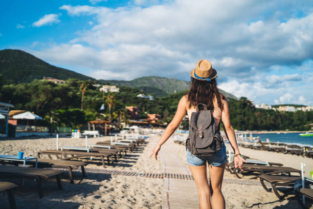 Young caucasian slim woman walking on beach among deck chairs.