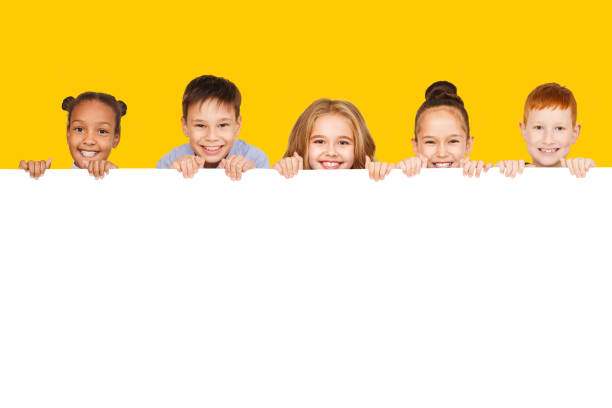 glückliche kinder mit leerem brett, gelbem hintergrund - spruchband fotos stock-fotos und bilder