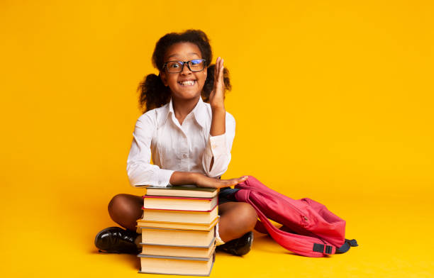 istock Black Elementary School Girl Raising Hand Sitting At Book Stack 1172147142