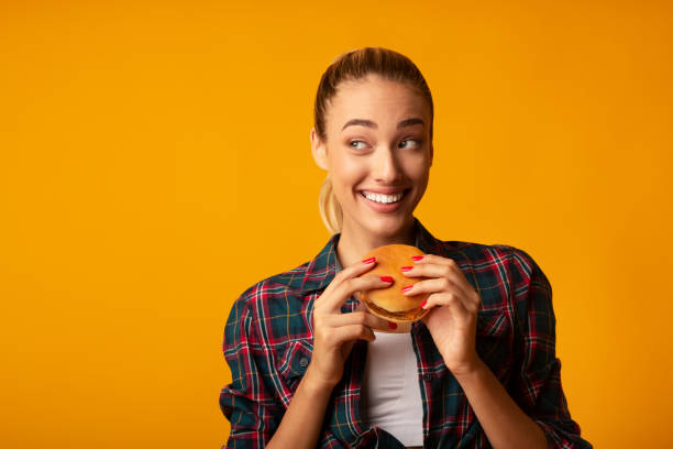 istock Young Lady Eating Hamburger Over Yellow Background 1172149508