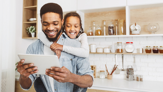Afro Dad And His Cute Daughter Having Video Call On Tablet, spending time together at kitchen, free space