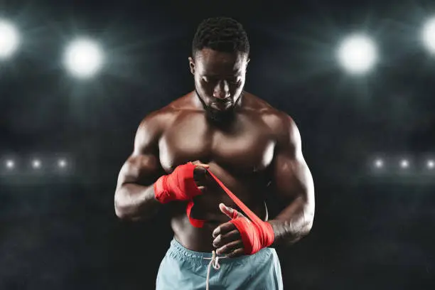 Photo of Professional black boxer wrapping hands before fight