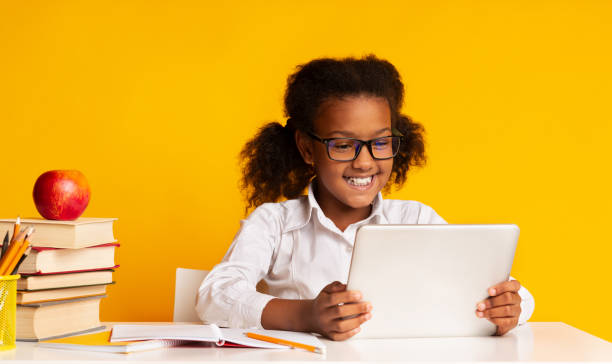 istock Afro Schoolgirl Using Tablet Sitting At Desk, Yellow Background 1172152211