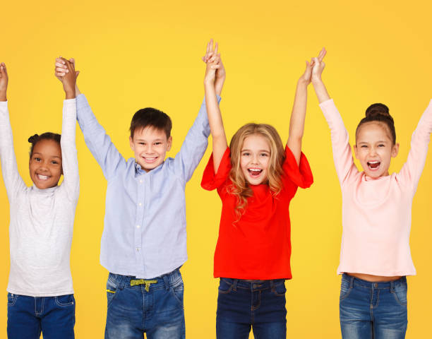 istock Happy school children raised hands together, yellow background 1172152310