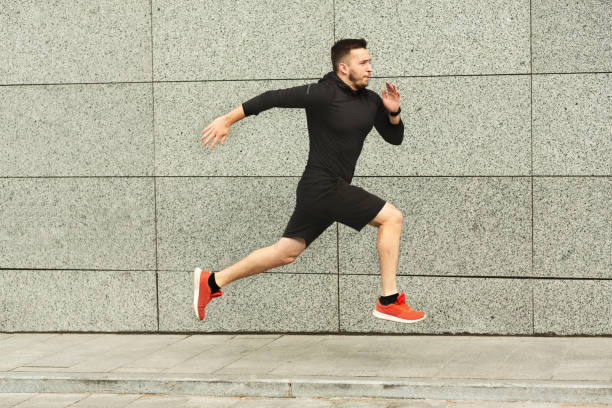 istock Young man jogging in city against grey urban wall, copy space, side view 1172152398