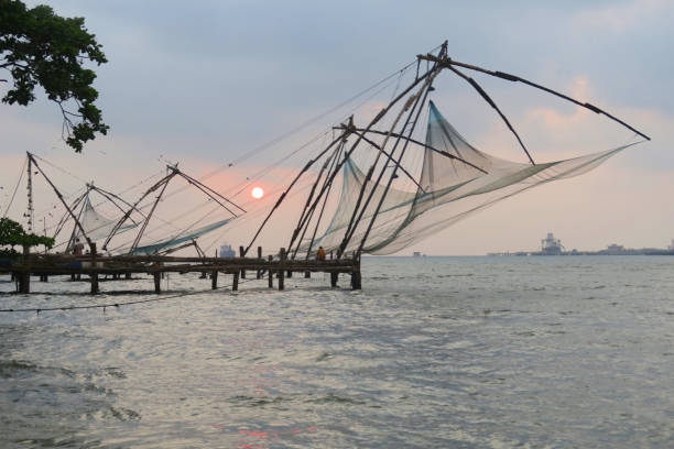 Stock photo of Chinese fishing nets at sunset in Fort Kochi beach in Cochin, Kerala, South India with local Indian fisherman catching tuna fish mackerel from port of Kochi harbour water in Indian Ocean / Arabian Sea, Cheena vala Chinese fishing nets Kochi photo imagen de las redes de pesca chinas al atardecer en la playa de fort kochi en cochin, kerala, al sur de la india con pescador indio local capturando caballa de atún desde el puerto de aguas del puerto de kochi en el océano indico / mar arábigo, cheena v