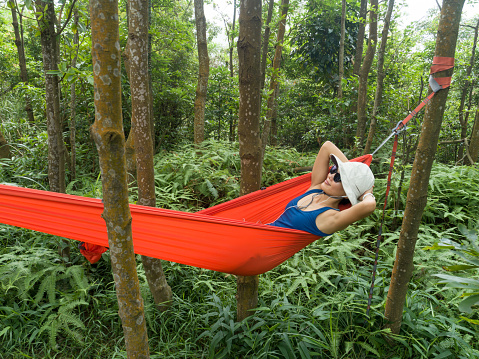 Woman relaxing in hammock listening music with smartphone in tropical rainforest