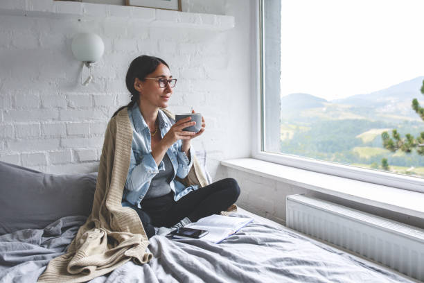 Woman sitting comfortable drinking tea and looking through window stock photo