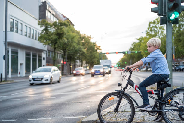 le garçon avec le vélo attend au feu de circulation d'une grande route - child bicycle cycling danger photos et images de collection