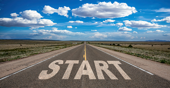 Start, new beginning concept. Text sign on a long straight highway in the american desert, blue cloudy sky background