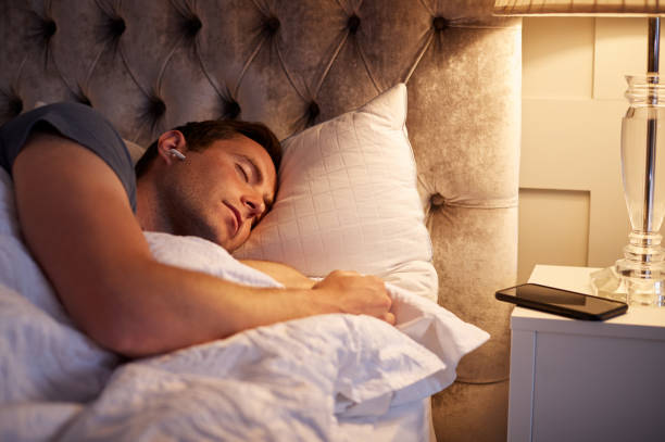 istock Man Sleeping In Bed Wearing Wireless Earphones Connected To Mobile Phone On Bedside Table 1172169515