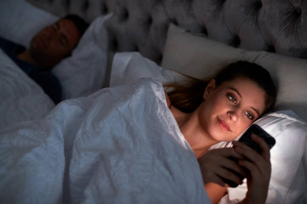 istock Woman Lying In Bed Checking Mobile Phone Whilst Man Sleeps Next To Her 1172170079