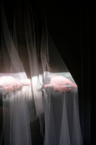 istock someone or something covered with a white veil shows their open hands with palms up lit by a halo of light in the dark 1172170580