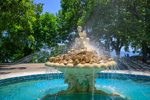 Fountain with angels statue in a sea garden park with grass and trees around it in Varna, Bulgaria.