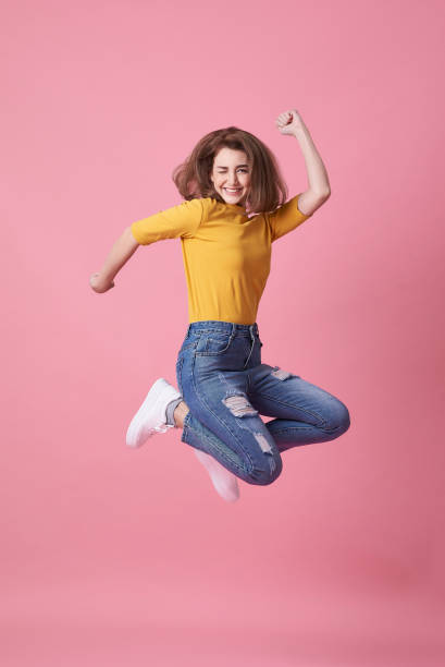 portrait of a joyful young woman in yellow shirt jumping and celebrating over pink background. - 2554 imagens e fotografias de stock