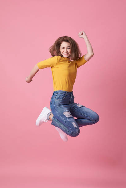 портрет радостной молодой женщины в желтой рубашке, прыгая и празднуя на розовом фоне. - 2554 стоковые фото и изображения