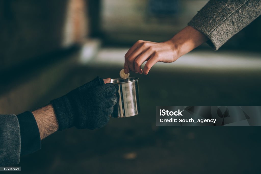 A helping hand One man, young homeless on the street begging, woman handing him some money, part of Begging - Social Issue Stock Photo
