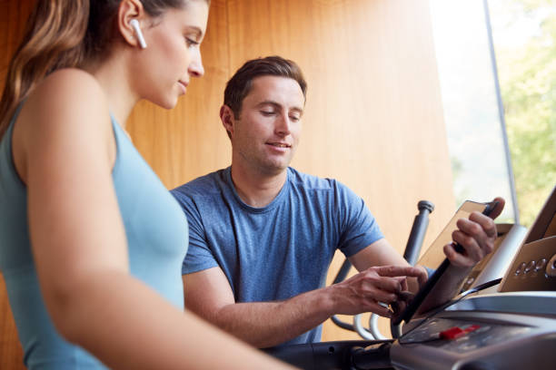 Woman In Gym With Personal Trainer Analysing Performance Using Smart Watch And Digital Tablet Woman In Gym With Personal Trainer Analysing Performance Using Smart Watch And Digital Tablet treadmill photos stock pictures, royalty-free photos & images