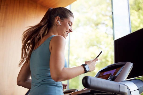 무선 이어폰과 스마트 워치를 착용하고 러닝머신에서 운동하는 여성 - treadmill 뉴스 사진 이미지