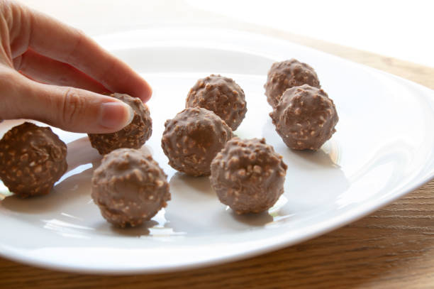 female hand tries round chocolate candy with nuts