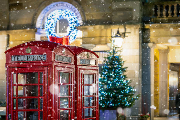 Red telephone booths in front of Christmas decorations lights in London, United Kingdom Classic, red telephone booths with snow falling in front of Christmas decorations lights in the Covent Garden area, London, United Kingdom winter wonderland london stock pictures, royalty-free photos & images