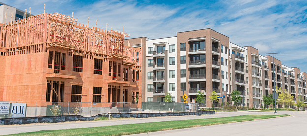 Panorama view street side development neighborhood with rental units under construction in North Dallas, Texas, USA. Wooden framework of five-story apartment large patio near completed buildings