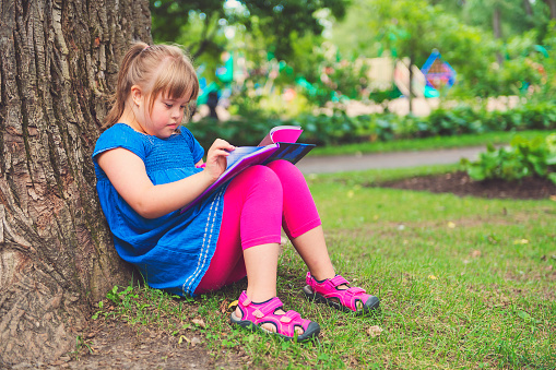 portrait of trisomie 21 child girl outside having fun on a park reading book