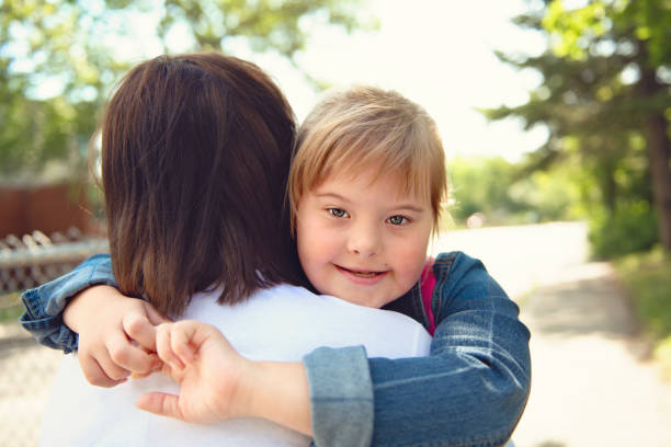 un portrait de trisomie 21 enfant fille à l'extérieur étreignant sa mère sur une cour de récréation d'école - child cheerful little girls down syndrome photos et images de collection