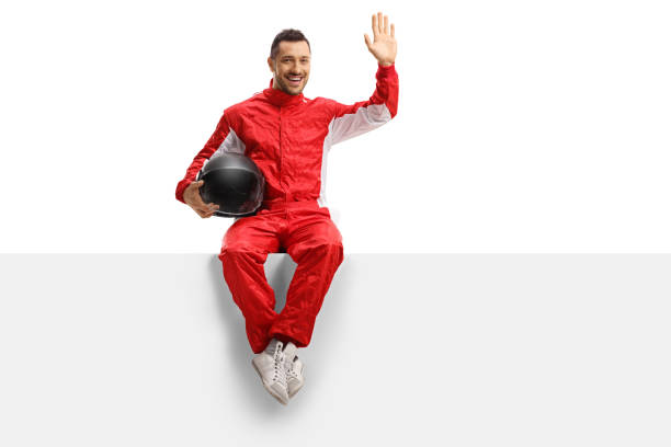 istock Young man racer in a red uniform sitting on a panel and waving 1172191251