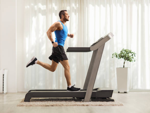 Young man running on a treadmill at home Full length profile shot of a young man running on a treadmill at home treadmill stock pictures, royalty-free photos & images