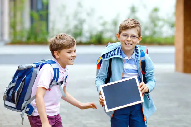 Two little kid boys with backpack or satchel. Schoolkids on the way to school. Healthy children, brothers and best friends outdoors on street leaving home. School's out on chalk desk. Happy siblings