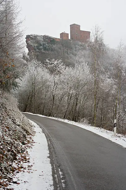 A castle on top of a steep rock, a road in the foreground.