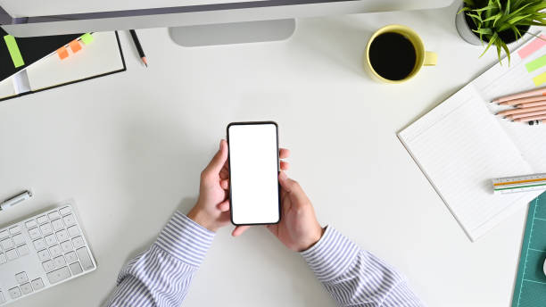 istock Man's hands holding smartphone mockup empty screen on office desk with Top view. 1172205590