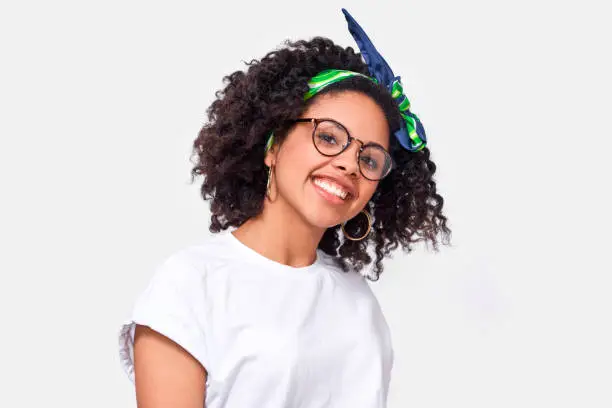 Beautiful happy dark-skinned young woman dressed in white t-shirt, enjoying the weather. African American female smiling broadly, wearing round eyewear posing over white studio wall