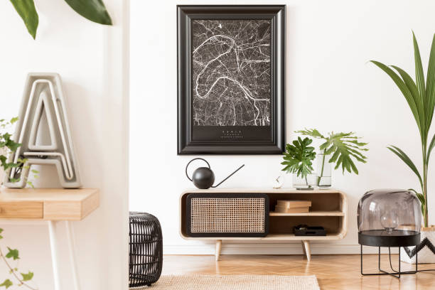 istock Modern scandinavian living room interior with black mock up poster map frame, desk, design wooden commode, plants, tropical leaf, books, lamp and elegant accessories. Template. Stylish home decor. 1172206878