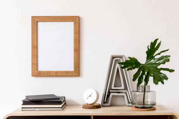 istock Modern home interior design with mock up photo frame, wooden commode, books, tropical leaf, big letter, white clock and elegant accessories. Stylish home decor. Template. Mockup ready to use. 1172206898