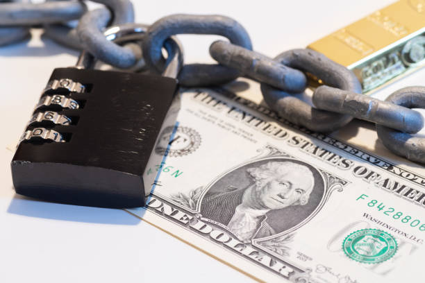 US Dollar banknote under metallic chain with padlock and gold bar in background