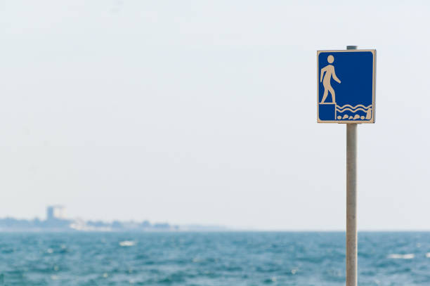 Shallow water sign on the beach in Croatia and wavy sea in background. Vacations, travel, swimming and safety concepts