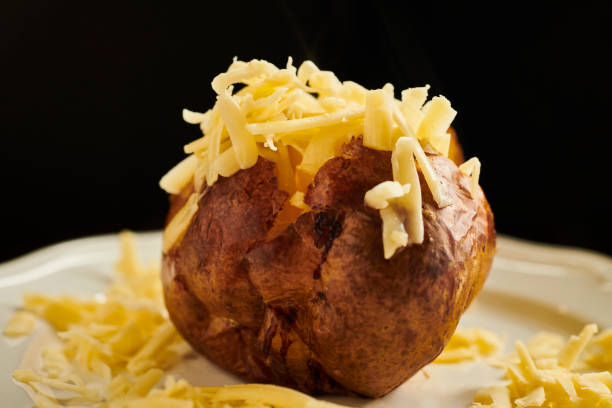 istock Baked Potato sliced open filled with grated cheddar cheese served on a white plate. 1172210154