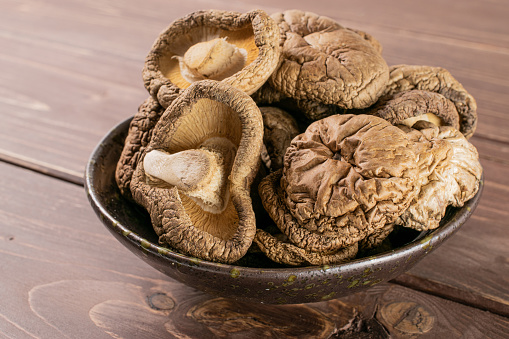 Lot of whole dry mushroom shiitake on grey ceramic plate on brown wood