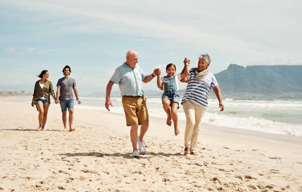 Grandkids keeps the heart young Shot of an adorable little girl having a fun day at the beach with her parents and grandparents swinger photo stock pictures, royalty-free photos & images