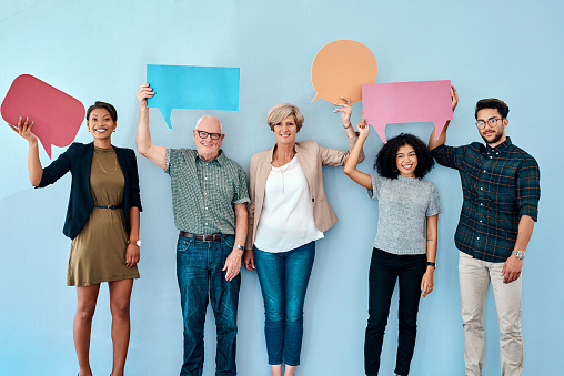 Shot of a diverse group of businesspeople holding up speech bubbles against a blue background
