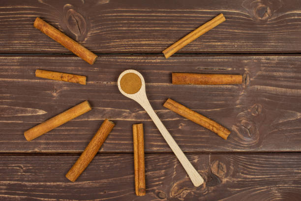 Group of eight whole dry brown cinnamon in a wooden spoon flatlay on brown wood