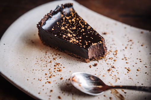 High angle shot of a home made chocolate and creamed nuts cake with elegant decorations on top of the coating, leaf shaped ornaments made of dark chocolate added to the decorations. Displayed on white ceramic serving plate.