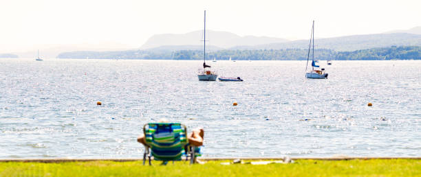 Panoramic view of Lake Memphremagog from Magog in Quebec's Eastern townships Panoramic view of Lake Memphremagog from Magog with sailboats in Quebec's Eastern townships on a sunny Summer day. An out of focus lawn chair is in the foreground. lake magog photos stock pictures, royalty-free photos & images