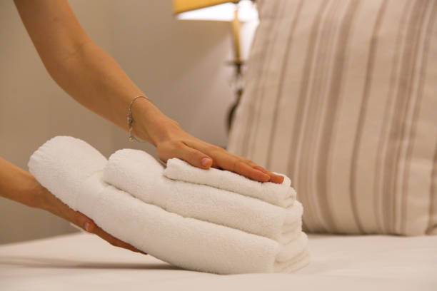service. femme changeant des serviettes dans la chambre d'hôtel. le nettoyeur de maison mettant des serviettes sur le lit, préparant tout pour que les clients emménagent dedans - lit rangée photos et images de collection