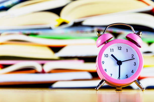 istock Pink alarm clock on background of stack of books 1172224413